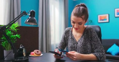 Akıllı telefon kullanan, kredi kartı tutan, masasında oturan, gülümseyen beyaz bir Amerikalı kadın.