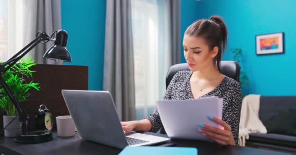 Una chica bonita joven trabaja con documentos mientras está sentada en un escritorio en un acogedor — Vídeos de Stock