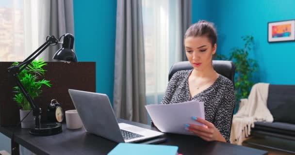 Ein junges hübsches Mädchen arbeitet mit Dokumenten, während sie an einem Schreibtisch in einem gemütlichen — Stockvideo