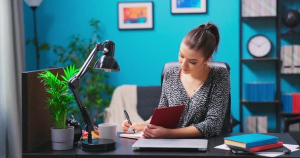 Eine junge hübsche Brünette arbeitet mit Dokumenten, während sie an einem Schreibtisch in einem — Stockvideo