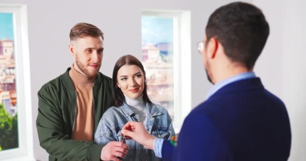 Житловий агент дає ключі для покупців нової квартири, щасливий чоловік і дружина — стокове відео