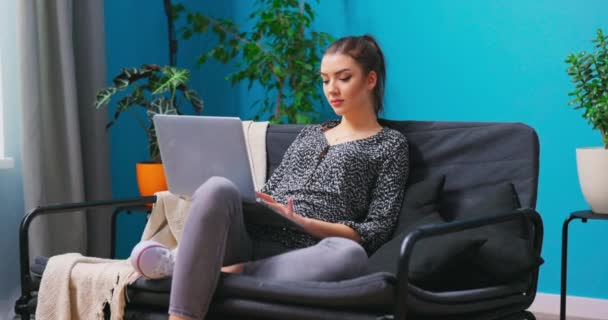 Sorrindo jovem mulher sentada no sofá usando notebook laptop olhando para mensagem de digitação de tela, feliz — Vídeo de Stock