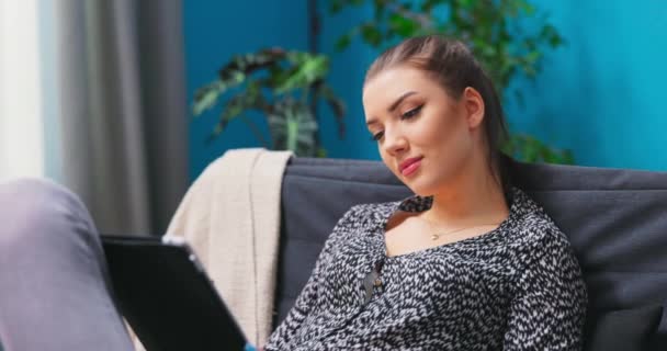 Mujer joven relajarse en acogedores muebles de sofá en la sala de estar mediante la navegación por Internet en la tableta, — Vídeo de stock