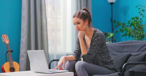 Een jonge vrouw ontspant zich op de bank in de woonkamer en gebruikt haar — Stockvideo