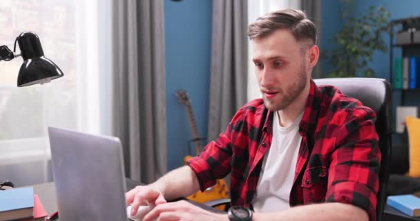 Un apuesto estudiante universitario está estudiando remotamente mientras está sentado en un escritorio en la vida — Vídeos de Stock