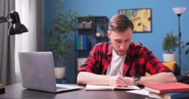 Bilgisayarda gülümseyen öğrenci sohbetleri. Kırmızı fanila giymiş bir genç.