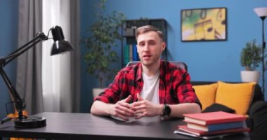 Bilgisayarda gülümseyen öğrenci sohbetleri. Kırmızı fanila giymiş bir genç.