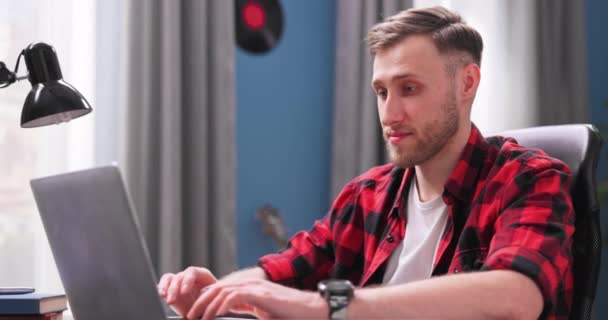 En stilig collegestudent studerar på distans medan han sitter vid ett skrivbord i livet — Stockvideo