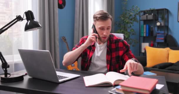 Przystojny młodzieniec siedzi przy biurku i rozmawia przez telefon.. — Wideo stockowe