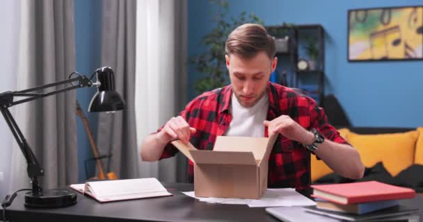 Mladý vysokoškolák vybalí balíček. Šťastný mladý muž otevře kartónovou krabici — Stock video