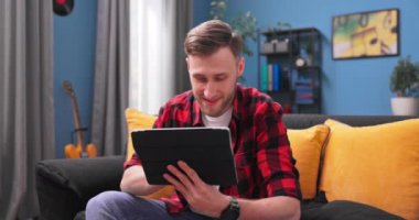 Gülümseyen genç öğrenci evde dijital tablet kullanıyor, milenyum erkek kullanıcı bilgisayar arıyor