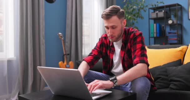 Un bel ragazzo studente universitario sta studiando a distanza mentre si siede sul divano in soggiorno — Video Stock