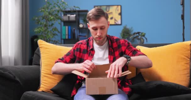 Мальчик-подросток распаковывает пакет. Счастливый молодой человек открывает картонную коробку — стоковое видео