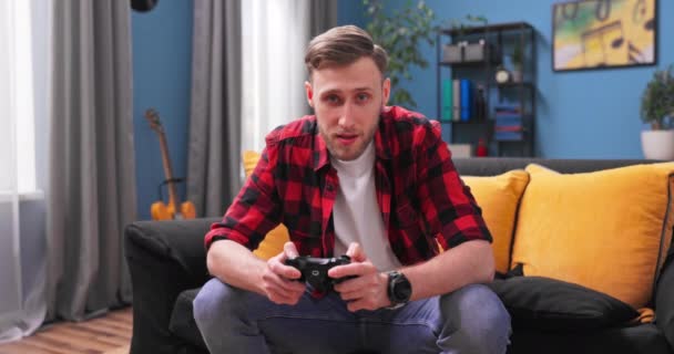 Glada amerikanska mannen vilar i rummet sitter på soffan spela TV-spel med hjälp av joysticks. Spelare — Stockvideo