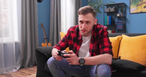 Tonåring student pojke spelar spel med joystick, njuter av att sitta på soffan i vardagsrummet på — Stockvideo