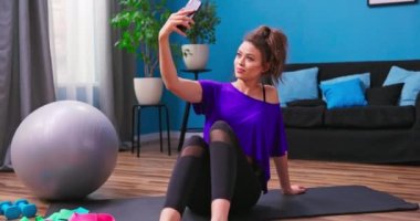 Spor kıyafetleri giymiş güzel bir kadın ahşap bir zeminde oturuyor.