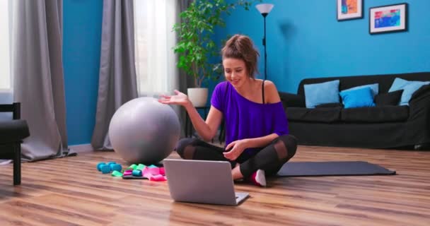 En söt ung kvinna klädd i fitness kläder chattar på en videochatt på en — Stockvideo