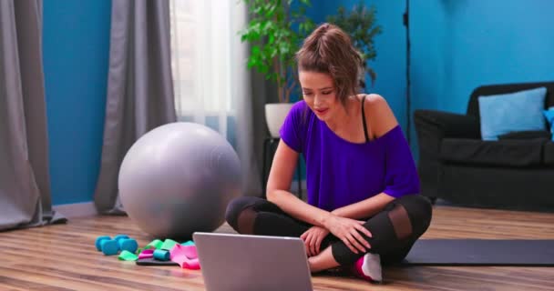 Een mooie jonge vrouw gekleed in fitness kleding chats op video chat met een persoonlijke — Stockvideo