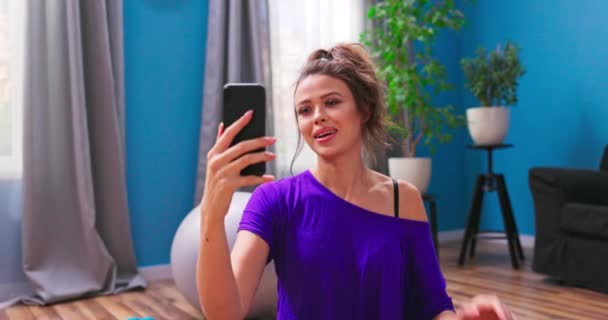 Mooie jonge vrouw gekleed in fitness kleding chats op video chat met een personal trainer — Stockvideo