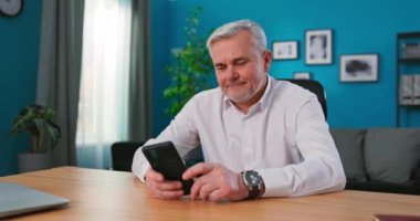 Mutlu orta yaş 55 'ler erkek kullanıcı akıllı telefon tutuyor cep telefonu videosu izliyor ve internetten arıyor