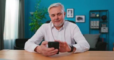 Kapalı mekanda oturan yaşlı adam cep telefonu ve kredi kartı ile başarılı bir ödeme yapar.,