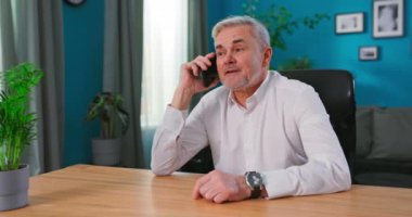 Yaşlı gri saçlı 55 'li yaşlarda bir adam evinde oturmuş akıllı telefon tutuyor ve keyifli sohbetlerin tadını çıkarıyor. Eski nesil