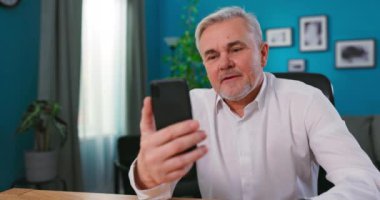 Orta yaşlı mutlu bir adamın portresi görüntülü konuşma yapıyor akıllı telefon ve torunlarla sohbet ediyor.