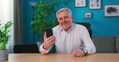 Gülümseyen büyükbaba cep telefonuyla aile hayatı paylaşımı sohbetinden zevk alıyor. Çok neşeli olgun bir adam.