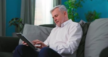 Gülümseyen yaşlı adam evde dijital tablet bilgisayar kullanarak konuşuyor.