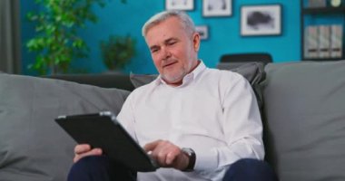 Odaklanmış orta yaşlı büyükbaba kanepede dinleniyor, web sörfü sağlık bilgileri dijital bilgisayarda