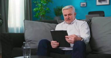 Mutlu yaşlı büyükbaba dijital tablet video konferansı düzenliyor. Sosyal mesafenin keyfini çıkarıyor.