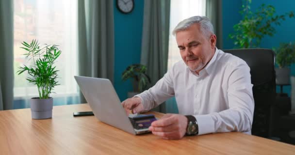 Зрелый 50-х человек сидеть за столом с помощью ноутбука делает покупки в Интернете электронной коммерции розничных сайтов, — стоковое видео