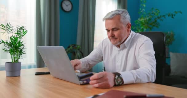 Boldog érett férfi használ laptop vásárlás online költőpénz hitelkártyára mobil banki alkalmazás — Stock videók