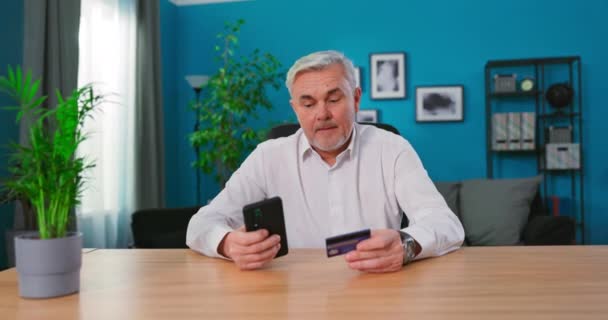 Зрелый 50-х человек сидеть за столом с помощью смартфона делает покупку в Интернете электронной коммерции розничной — стоковое видео