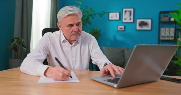 Ezüst hajú üzletember, jegyzetekkel a füzetében. Idősek főnöke a munkahelyen — Stock videók