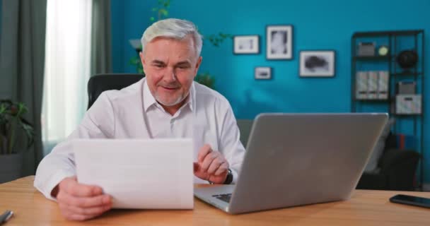 Щасливий серйозний старий зрілий чоловік читає медичний звіт, працює з паперовими документами, сидячи в — стокове відео
