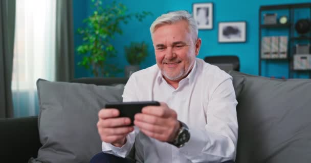 白人老人在家里客厅里用手机玩游戏。老年人家庭 — 图库视频影像