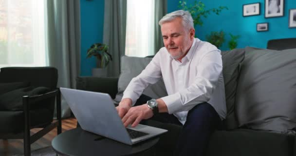 Χαμογελώντας χαρούμενος μεσήλικας 50άρης ανώτερος άνθρωπος χρησιμοποιώντας την τεχνολογία υπολογιστών laptop που εργάζονται σε απευθείας σύνδεση, surfing — Αρχείο Βίντεο