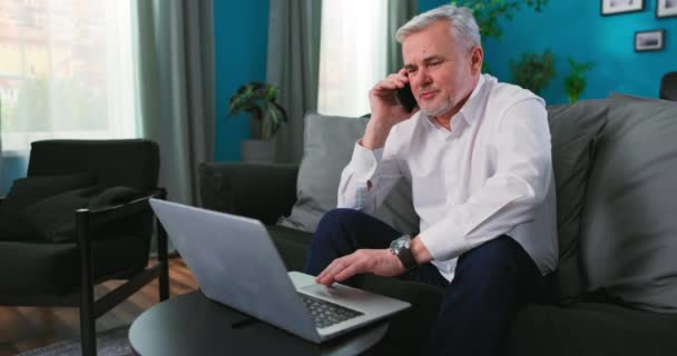 Homem de negócios de meia idade velho que trabalha com laptop, homem maduro sênior ocupado falando com banco sobre — Vídeo de Stock