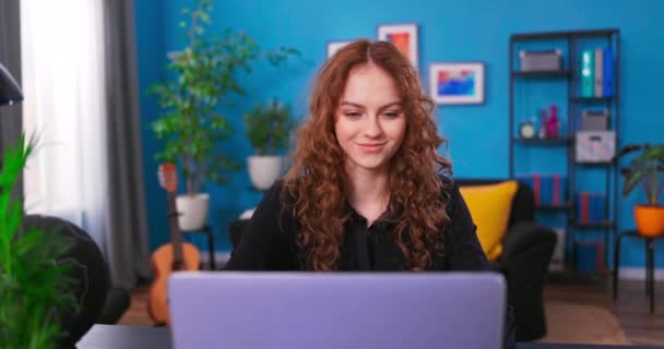 Een jonge tienervrouw studeert met een laptop in haar slaapkamer. Mooie vrouw chatten met — Stockvideo