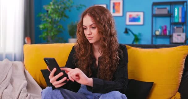 Retrato de una hermosa adolescente caucásica con el pelo rizado en la acogedora sala de estar usando — Vídeo de stock
