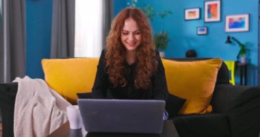 Gülümseyen genç kadın dizüstü bilgisayarını kullanarak koltukta oturuyor ekran daktilo mesajına bakıyor, mutlu.