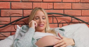 Güzel hamile bir kadın evde yatakta uzanıyor ve bir telefon görüşmesi yapıyor.