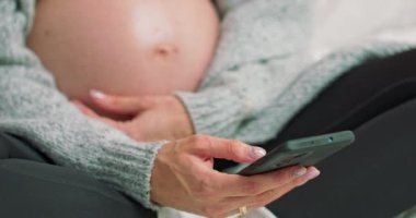 Genç hamile kadın telefonları kaydırıyor. İnternette sörf yapmak. Şefkatli bir anne, çıplak bir hamile kadını okşar.