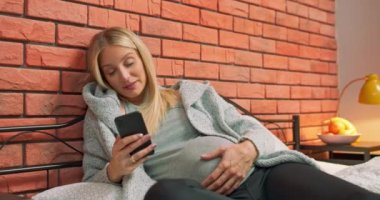 Mutlu hamile genç kadın akıllı telefon kullanarak kocasına ya da ailesine mesaj atıyor.