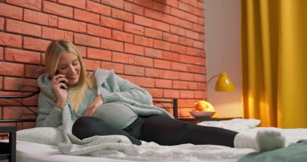Mladá těhotná žena leží na posteli mluví se svým manželem pomocí telefonu na — Stock video