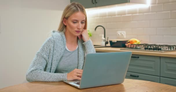 Retrato da jovem mãe grávida sentada na mesa da cozinha e assistindo a algo — Vídeo de Stock