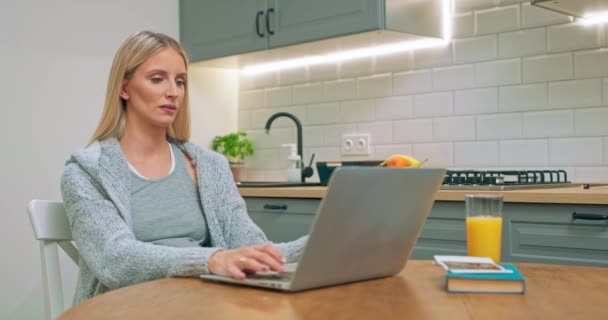 Mulher grávida trabalhando no computador portátil sentado na mesa da cozinha e bebendo suco — Vídeo de Stock