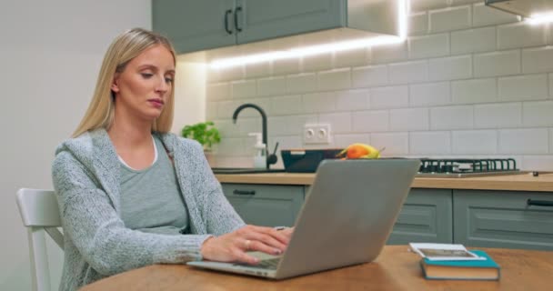 Szomorú és fáradt terhes nő dolgozik a laptop számítógép ül a konyhaasztalnál — Stock videók