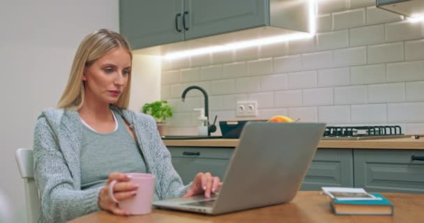 Portret foto van de jonge zwangere moeder zitten aan de keukentafel en kijken naar iets — Stockvideo